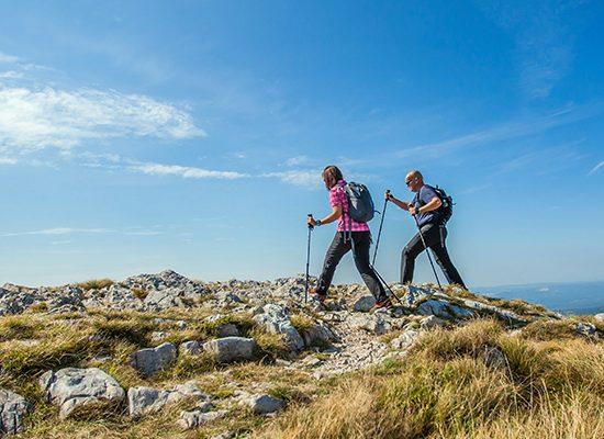 couple hiking on nanos plateau in slovenia against a blue sky