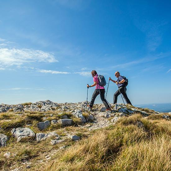 couple hiking on nanos plateau in slovenia against a blue sky