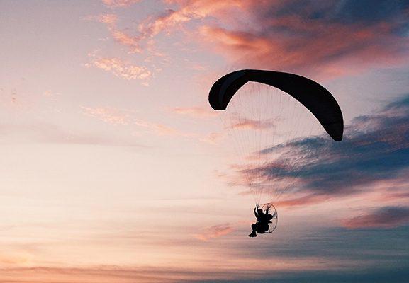 horizontal shot of a beach with a person gliding down on a paramotor parachute 1