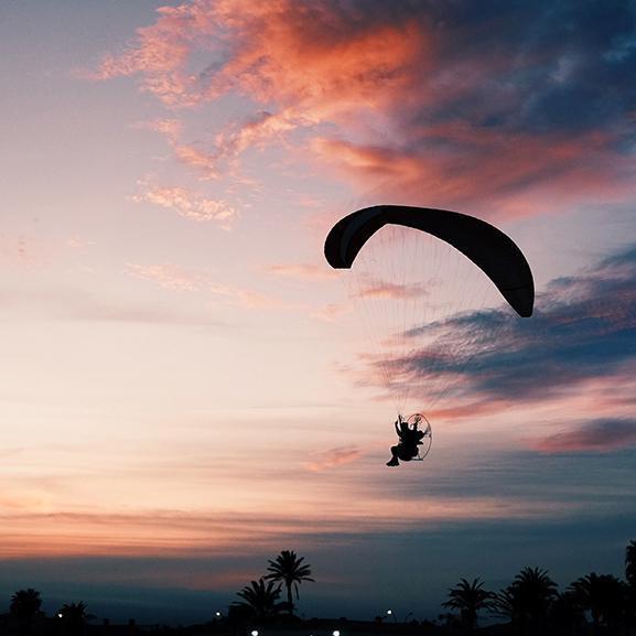 horizontal shot of a beach with a person gliding down on a paramotor parachute 1
