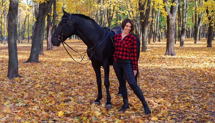 happy young woman next to black horse in autumn in the park